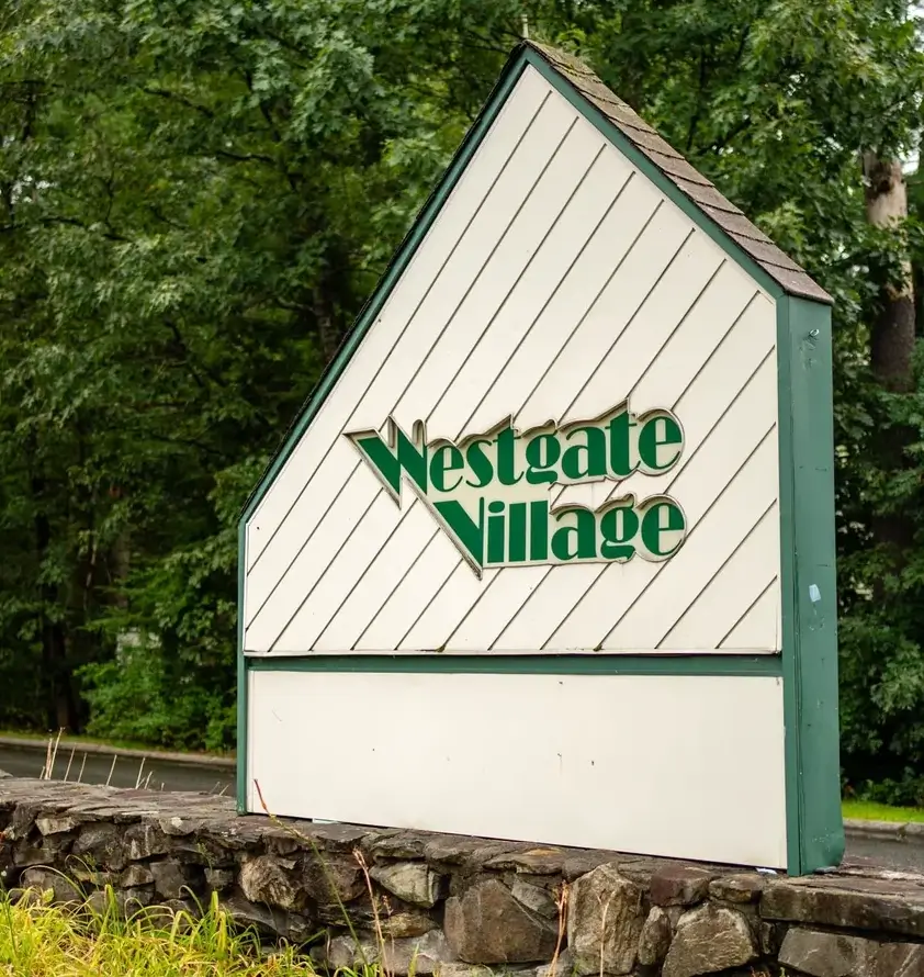 Sign reading "Westgate Village" amidst trees.